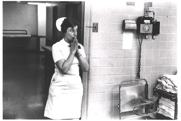 A nurse praying in the doorway of a hospital ward