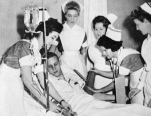 A young male patient receives plenty of attention from students and instructor.	School of Nursing Catalog, The Record, 1963-64.